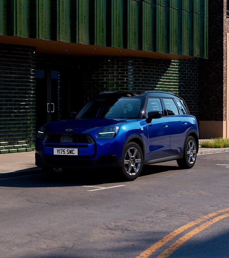 A blue MINI Countryman is parked outside a building, highlighting its stylish appearance and urban setting.